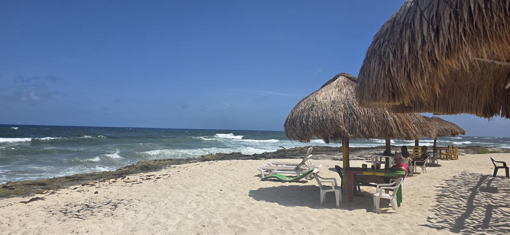 Thatched parasols and sun loungers on a quiet Caribbean beach beside turquoise surf