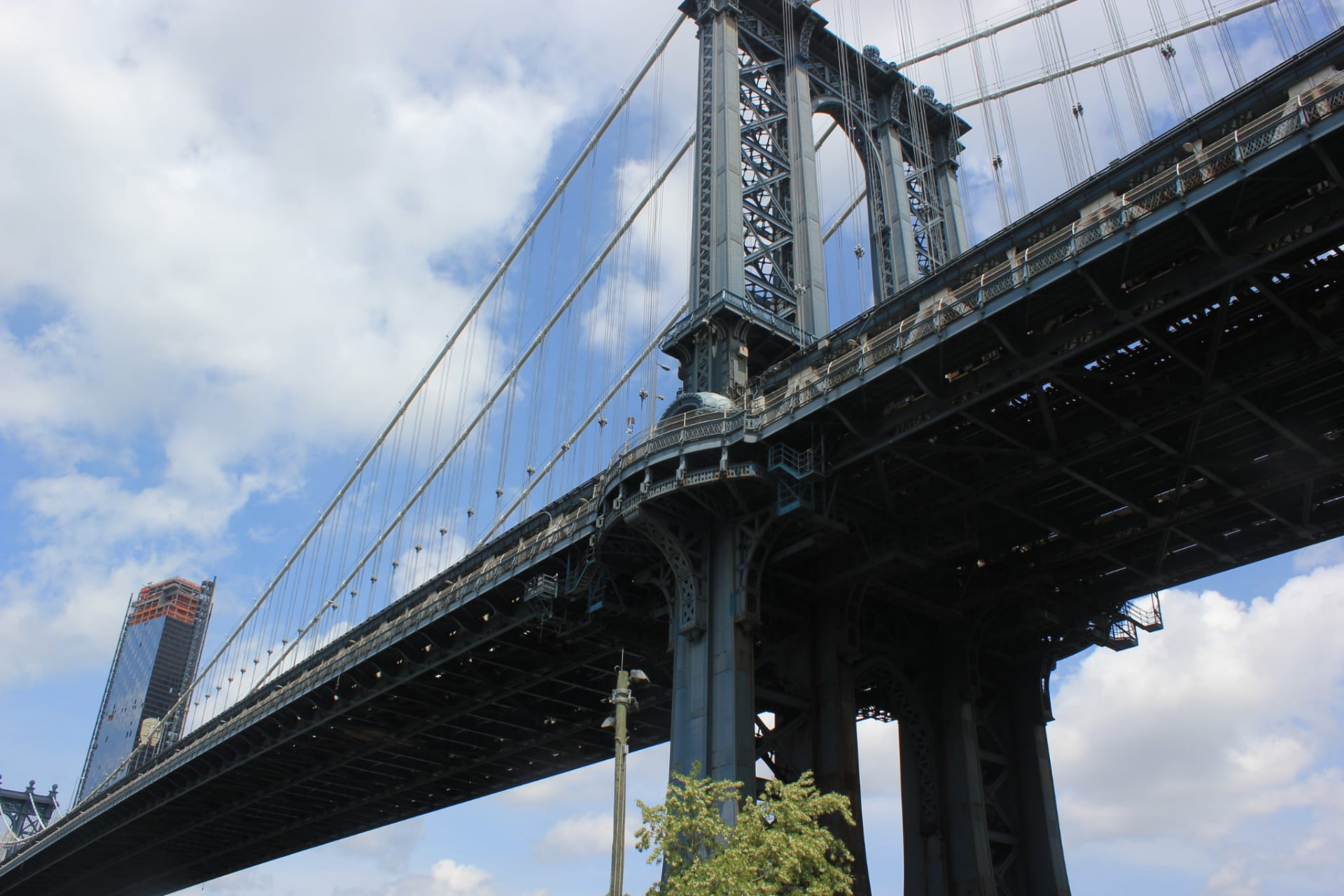 Looking up at the steelwork of Manhattan Bridge against a bright, cloudy sky